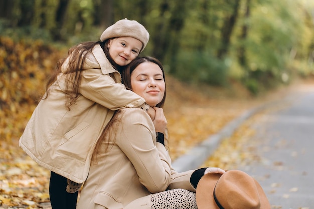 Retrato de feliz madre e hija pasando tiempo juntas en el parque de otoño con hojas amarillas cayendo