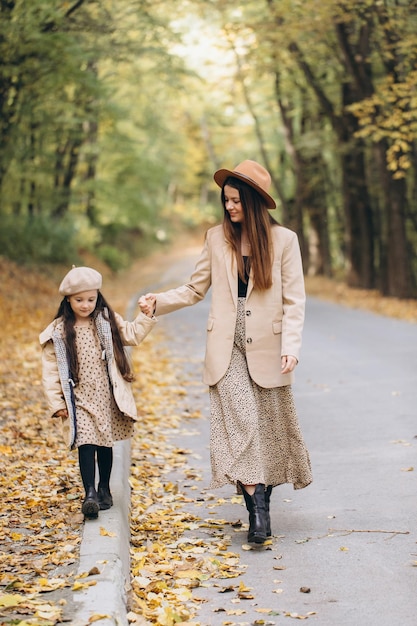 Retrato de feliz madre e hija pasando tiempo juntas en el parque de otoño con hojas amarillas cayendo