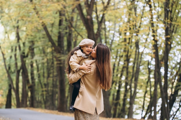 Retrato de feliz madre e hija pasando tiempo juntas en el parque de otoño con hojas amarillas cayendo