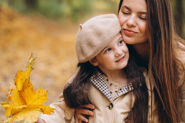 Retrato de feliz madre e hija pasando tiempo juntas en el parque de otoño con hojas amarillas cayendo