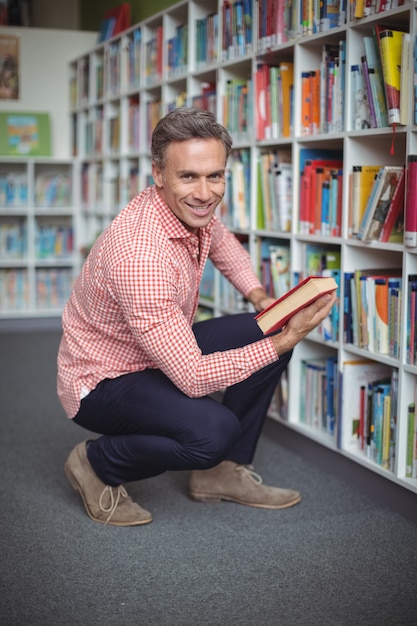 Retrato de feliz maestro de escuela seleccionando libro en biblioteca