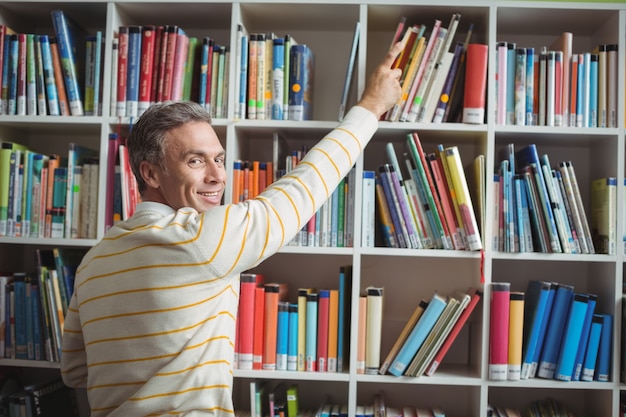 Retrato de feliz maestro de escuela seleccionando libro en biblioteca