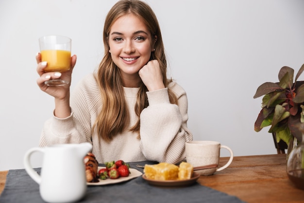 Retrato de feliz mujer caucásica vistiendo ropa casual sonriendo mientras desayuna en la acogedora habitación