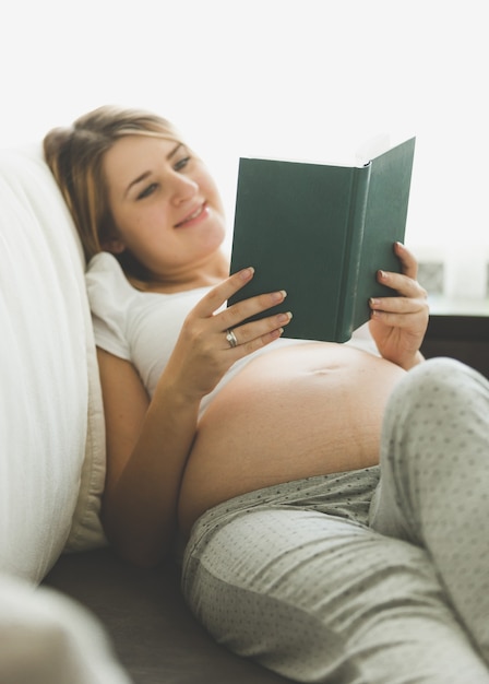 Retrato, de, feliz, mujer embarazada, libro de lectura, en, sofá, en, sala