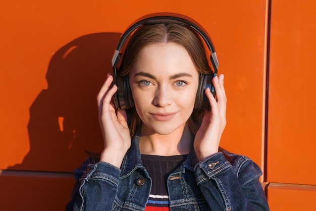 Retrato feliz mujer joven sonriente con auriculares escuchando música en naranja