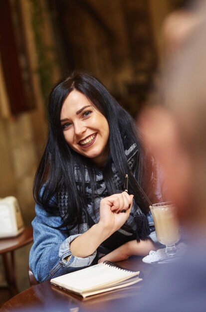 Retrato de feliz mujer de negocios informal con chaqueta sentada en su asiento en el café