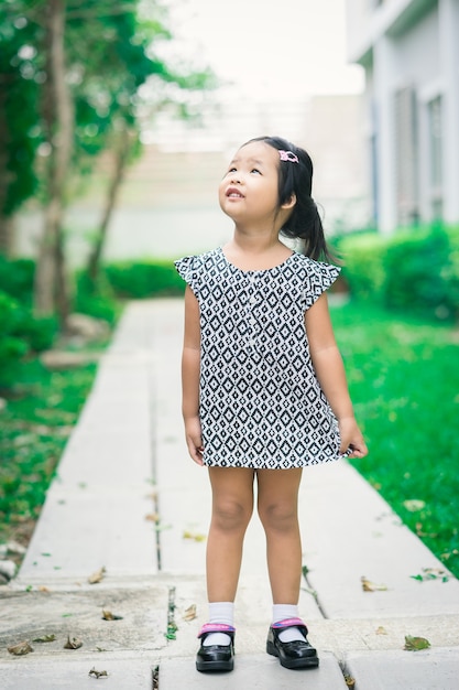 Retrato de feliz niña asiática en vestido de pie en el sendero en el parque