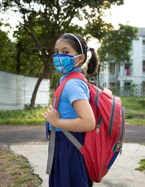 Foto retrato de una feliz niña india estudiante en uniforme escolar protección de máscara nasal yendo a la escuela