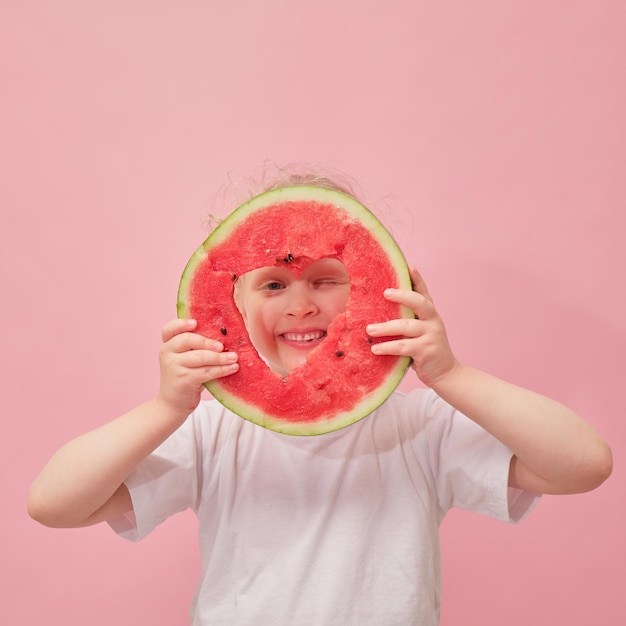 Retrato feliz niña pequeña está sosteniendo una rodaja de sandía sobre fondo rosa colorido