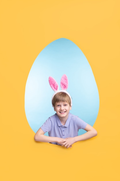 Retrato de feliz niño emocionado en la oreja diadema de liebre de pie en el marco en forma de huevo de Pascua