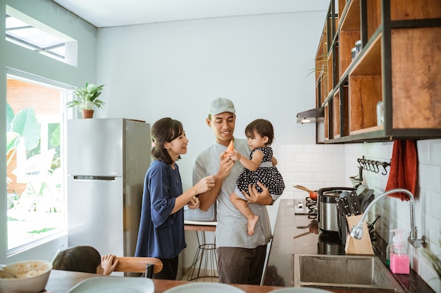 Retrato de feliz padre asiático, madre e hija cocinando juntos en la cocina moderna