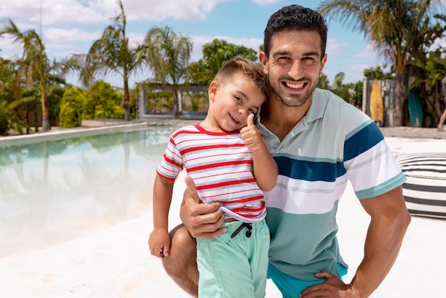 Foto retrato de feliz padre birracial e hijo abrazándose junto a la piscina. pasar tiempo de calidad, estilo de vida, familia, verano y concepto de vacaciones.