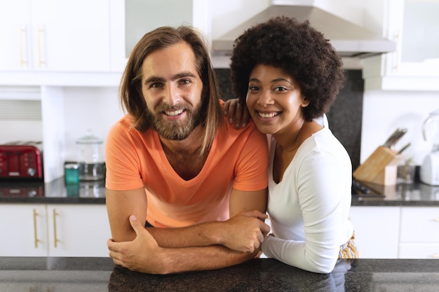 Retrato de una feliz pareja diversa en la cocina sonriendo y abrazando