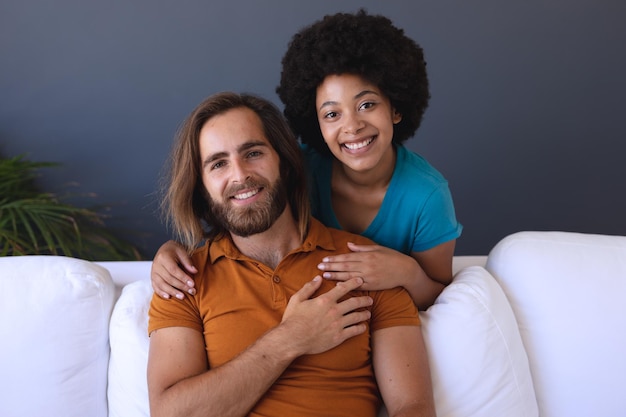 Retrato de una feliz pareja diversa sentada en un sofá abrazándose y sonriendo
