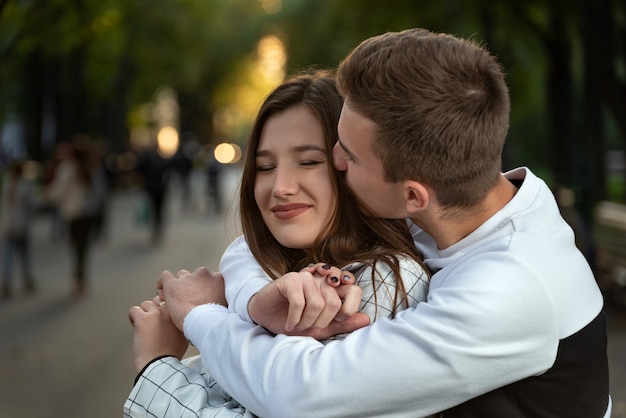 Retrato de la feliz pareja de enamorados en el parque. Guy abraza a su amada por los hombros y la besa.