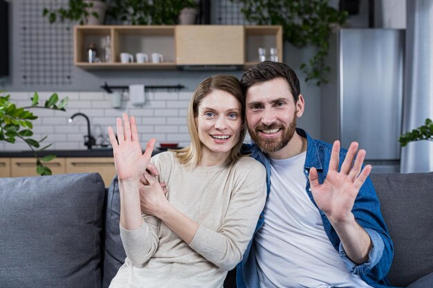 Retrato de una feliz pareja familiar joven Hombre y mujer sentados en el sofá abrazándose saludando sonriendo mirando a la cámara mirándose el uno al otro