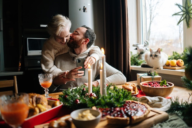 Retrato de la feliz pareja joven abrazándose sentados en la mesa festiva de Navidad durante las vacaciones en familia