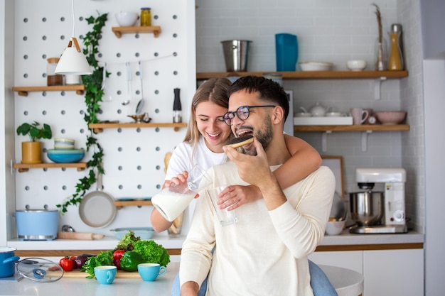 Retrato de feliz pareja joven cocinando juntos en la cocina en casa Linda pareja joven disfrutando de su desayuno juntos ella le está sirviendo leche