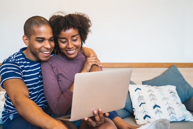 Retrato de feliz pareja joven relajante y usando la computadora portátil en el sofá en casa