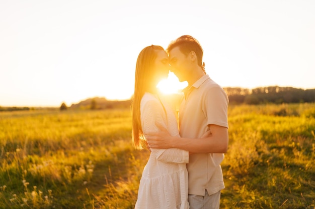 Retrato de una feliz pareja joven y sonriente enamorada abrazándose y besándose con los ojos cerrados disfrutando el uno del otro en un hermoso prado verde en las noches de verano