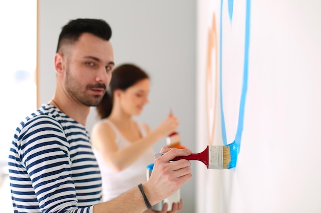 Retrato de feliz pareja joven sonriente pintando la pared interior de la nueva casa pareja joven