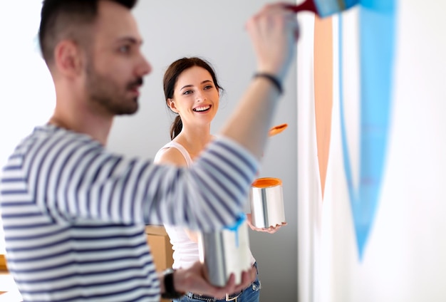 Retrato de feliz pareja joven sonriente pintando la pared interior de la nueva casa pareja joven