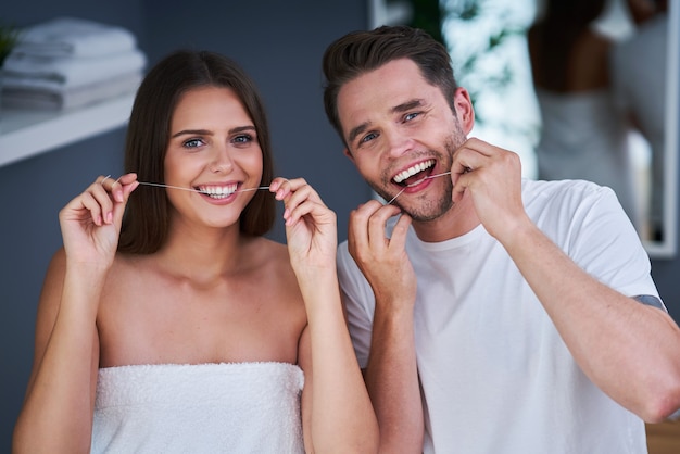 Retrato, de, feliz, pareja joven, usar hilo dental, dientes, en, el, cuarto de baño