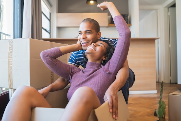 Retrato de feliz pareja latina divirtiéndose con cajas de cartón en casa nueva en el día de la mudanza. Concepto de bienes raíces.