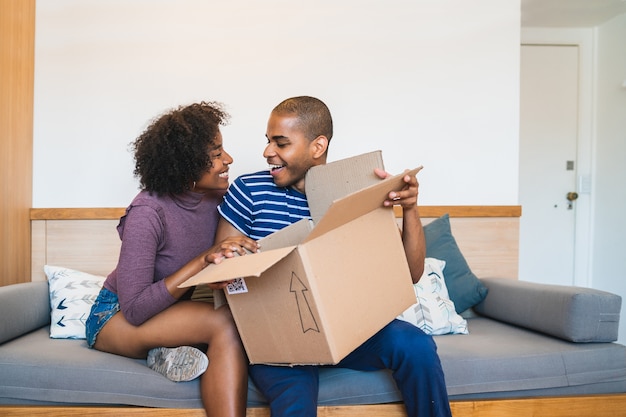 Retrato de la feliz pareja latina joven abriendo un paquete en casa