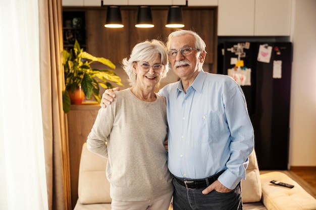 Retrato de una feliz pareja de mayores de pie en casa y sonriendo a la cámara