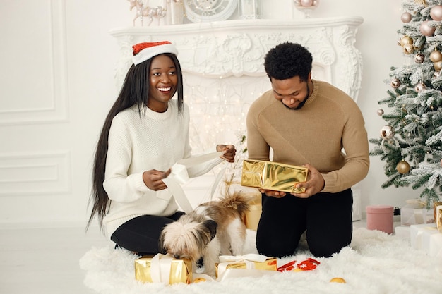 Retrato de una feliz pareja negra sosteniendo regalos y sentada cerca del árbol de Navidad