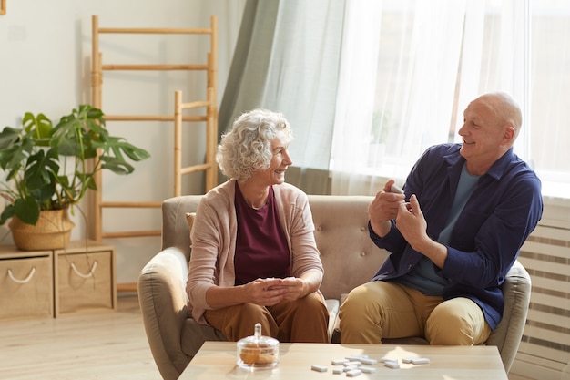 Retrato de la feliz pareja senior hablando emocionalmente mientras está sentado en el sofá en el acogedor interior de una casa iluminada por la luz del sol