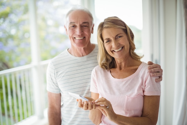 Retrato de la feliz pareja senior de pie en el balcón con teléfono móvil