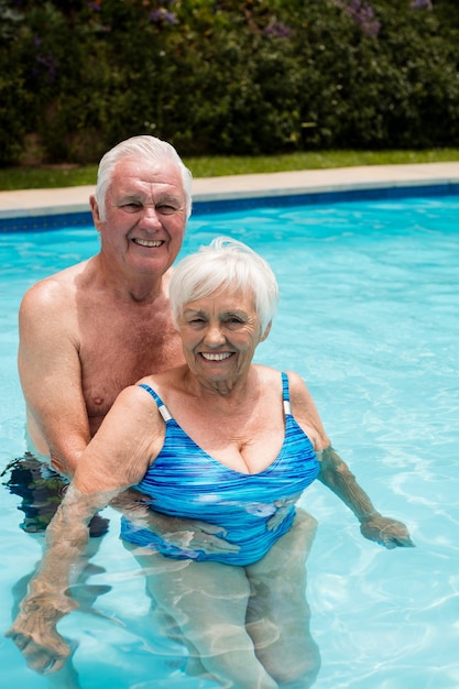 Retrato de la feliz pareja senior en la piscina en un día soleado