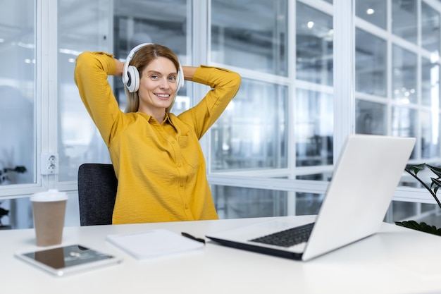 Retrato de una feliz programadora dentro de una trabajadora de oficina con una laptop y auriculares sonriendo