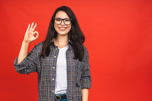 Retrato de feliz sonriente morena chica de negocios mujer en casual aislado sobre fondo rojo signo Ok