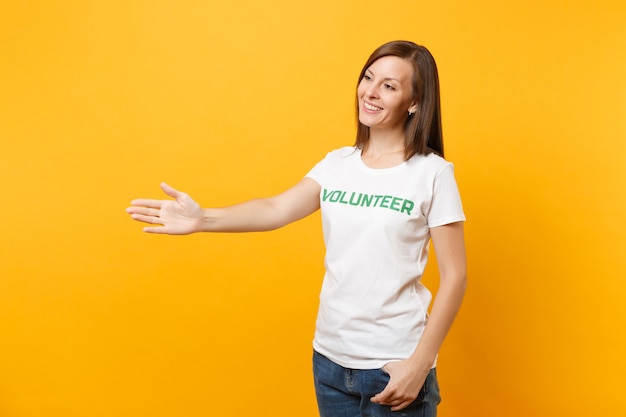 Retrato de feliz sonriente mujer satisfecha en camiseta blanca con inscripción escrita voluntario de título verde aislado sobre fondo amarillo. Ayuda de asistencia gratuita voluntaria, concepto de trabajo de gracia de caridad.