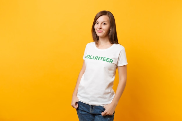 Retrato de feliz sonriente mujer satisfecha en camiseta blanca con inscripción escrita voluntario de título verde aislado sobre fondo amarillo. Ayuda de asistencia gratuita voluntaria, concepto de trabajo de gracia de caridad.