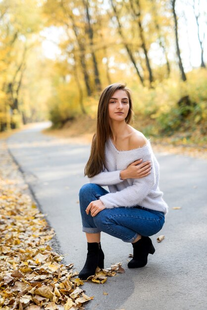 Retrato femenino. Mujer joven en ropa casual posando en el bosque de otoño con hojas amarillas