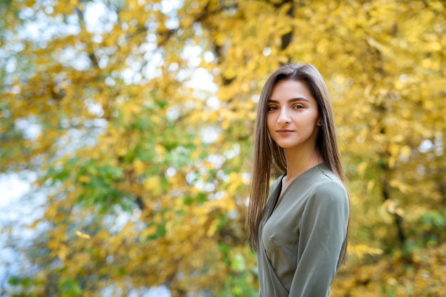 Retrato femenino. Retrato de mujer morena en el parque otoño con vestido verde oliva