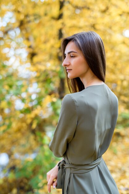 Retrato femenino. Retrato de mujer morena en el parque otoño con vestido verde oliva