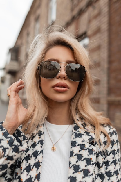 Retrato femenino urbano de una hermosa mujer sexy con gafas y labios grandes en un abrigo de moda caminando por la ciudad