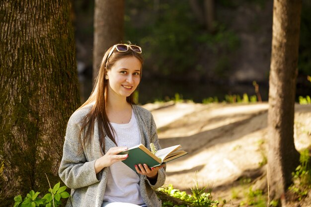 Retrato feminino de uma jovem mulher caucasiana em um parque com um livro nas mãos em um dia ensolarado