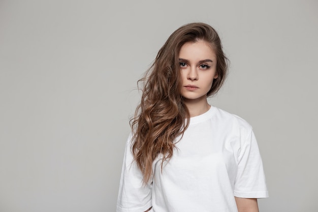 Retrato feminino de uma linda garota com um penteado em uma camiseta branca no estúdio olha para a câmera Mulher séria em fundo cinza