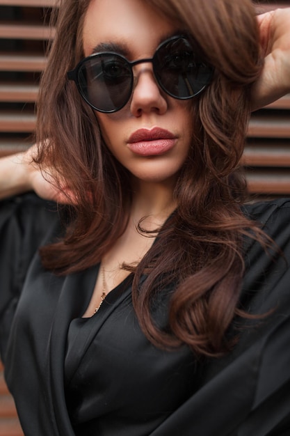 Foto retrato feminino glamoroso de uma bela jovem modelo morena com óculos de sol da moda em poses de vestido elegante na rua