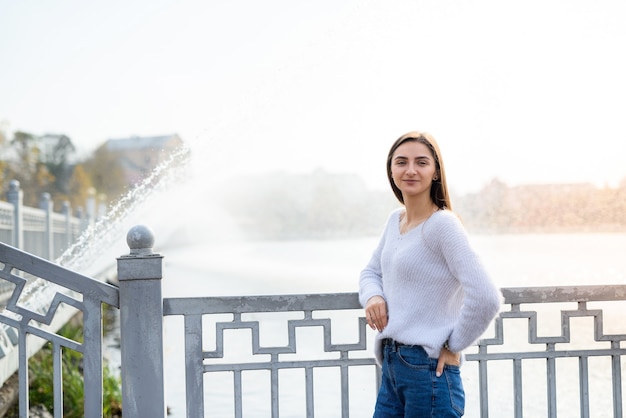 Retrato feminino. Mulher bonita em roupa casual posando na margem do lago com uma fonte