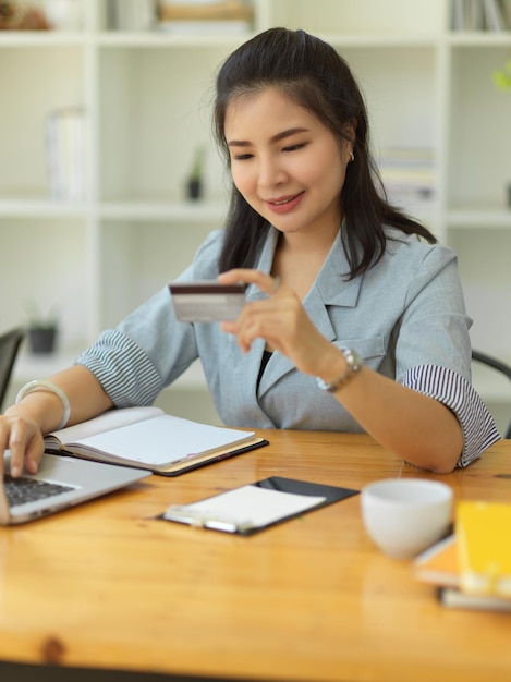 Retrato feminino pagando suas contas via transação online usando computador portátil segurando um cartão de crédito