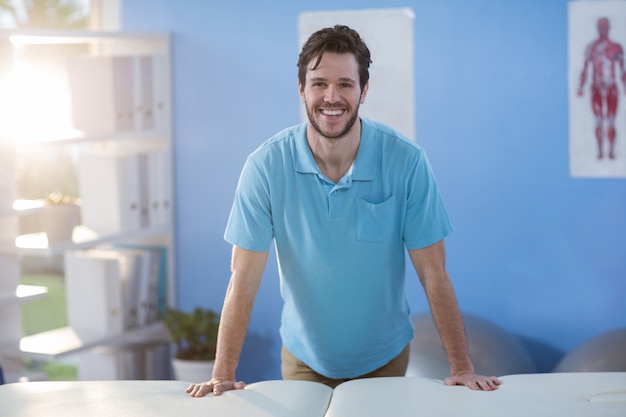 Foto retrato de fisioterapeuta masculino de pie cerca de la cama de masaje