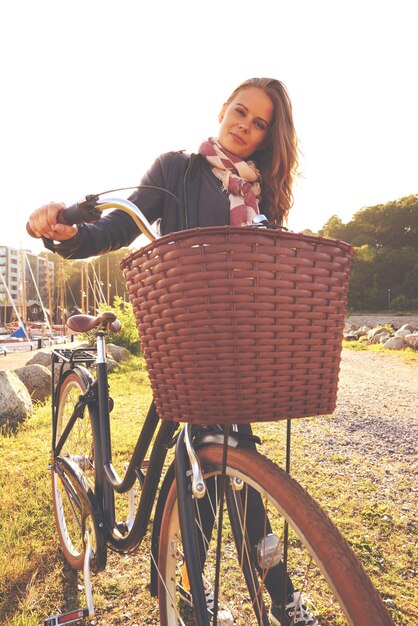 Foto retrato flare y una chica con su bicicleta en el parque para la libertad de viaje o la aventura ecológica ciclismo de verano y una persona joven al aire libre en el campo para un paseo en bicicleta con una canasta