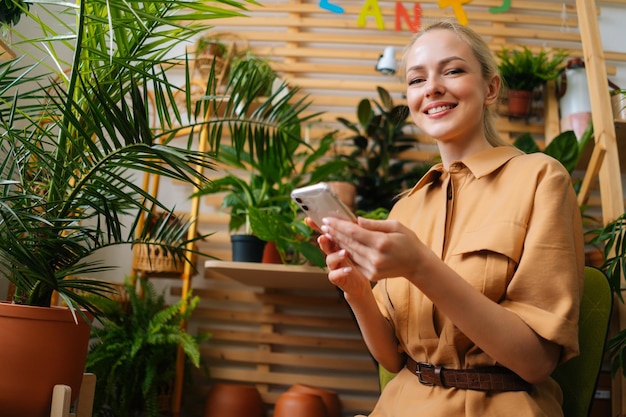 Retrato de una florista sonriente hablando en línea con un cliente usando un teléfono móvil en una tienda de flores mirando la cámara